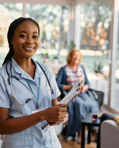 Young happy black nurse working at residential care home and looking at camera.